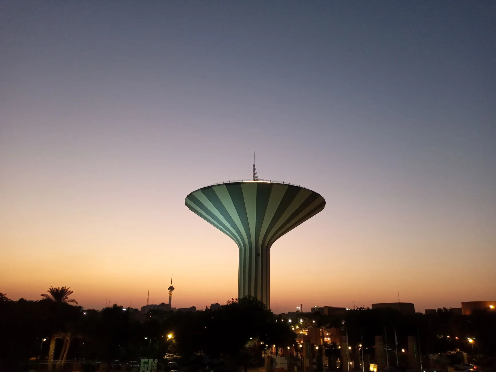برج المياه في الرياض عند الغروب، وخط أفق المدينة مضاءً تحته.